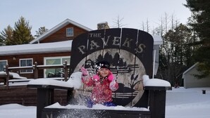 A snow-covered welcome sign with the text "The Peverels" and "WELCOME" in front of a wooden house. - Lake Pavek Lake (Elcho)