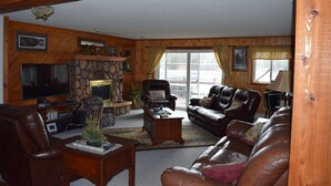 A cozy living room with a fireplace, leather sofas, a television, and a stone wall. - Lake Pavek Lake (Elcho)