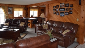 A cozy living room with leather sofas, a dining area, and a wall decorated with family photos. - Lake Pavek Lake (Elcho)