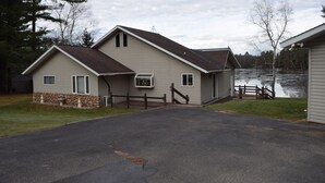 A two-story house with a stone foundation, a garage, and a driveway leading to a wooden dock over water. - Lake Pavek Lake (Elcho)