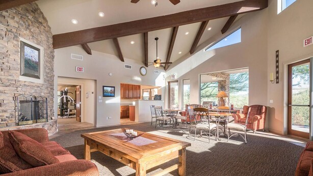 A spacious living area with a fireplace, a dining table, and comfortable seating. There is a kitchen area in the background with wooden cabinets and a large window. - Two Mountain Views in Gold Canyon (Gold Canyon)