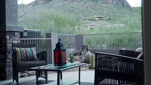 A patio with a stone wall, a wicker sofa, a table with a lantern, and cacti. - Two Mountain Views in Gold Canyon (Gold Canyon)