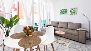 Un salon moderne avec un canapé beige, des chaises blanches, une petite table ronde et un saladier de fruits posé sur un set de table en fibres tressées.