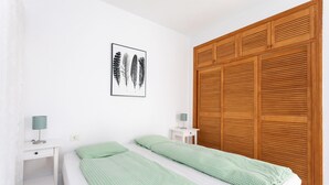 Une chambre à coucher comprenant un lit, deux tables de chevet, une armoire en bois, un tableau accroché au mur et une couvre-lit à motifs.