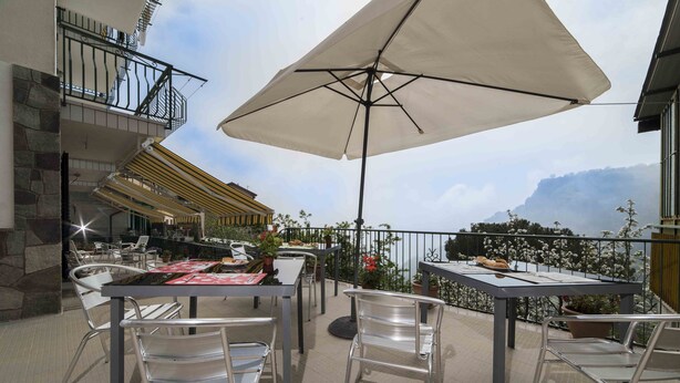 An outdoor patio with metal chairs and tables, a large umbrella, and a view of the mountains.