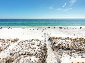 Relax on the beach with lounge chairs and umbrellas, surrounded by a tranquil sea and a scenic walkway.
