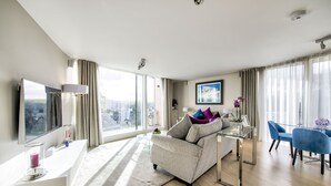 Una sala de estar moderna con un sofá, una mesa de centro de vidrio, un televisor y vistas a la ciudad a través de grandes ventanales.