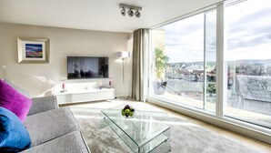 Una sala de estar moderna con una mesa de centro de vidrio, un sofá con cojines de colores, un televisor de pantalla plana y un ventanal con vista a la ciudad.