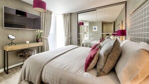 Habitación de hotel moderna con una cama grande, una mesita de noche, un espejo, un televisor y un espejo grande en la pared.