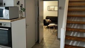 Una cucina compatta con forno a microonde, forno e pensili. Si intravede un'area pranzo con tavolo e sedie tramite una porta aperta.
