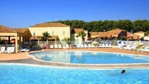 Una piscina con lettini e ombrelloni, circondata da edifici con tetti in tegole.
