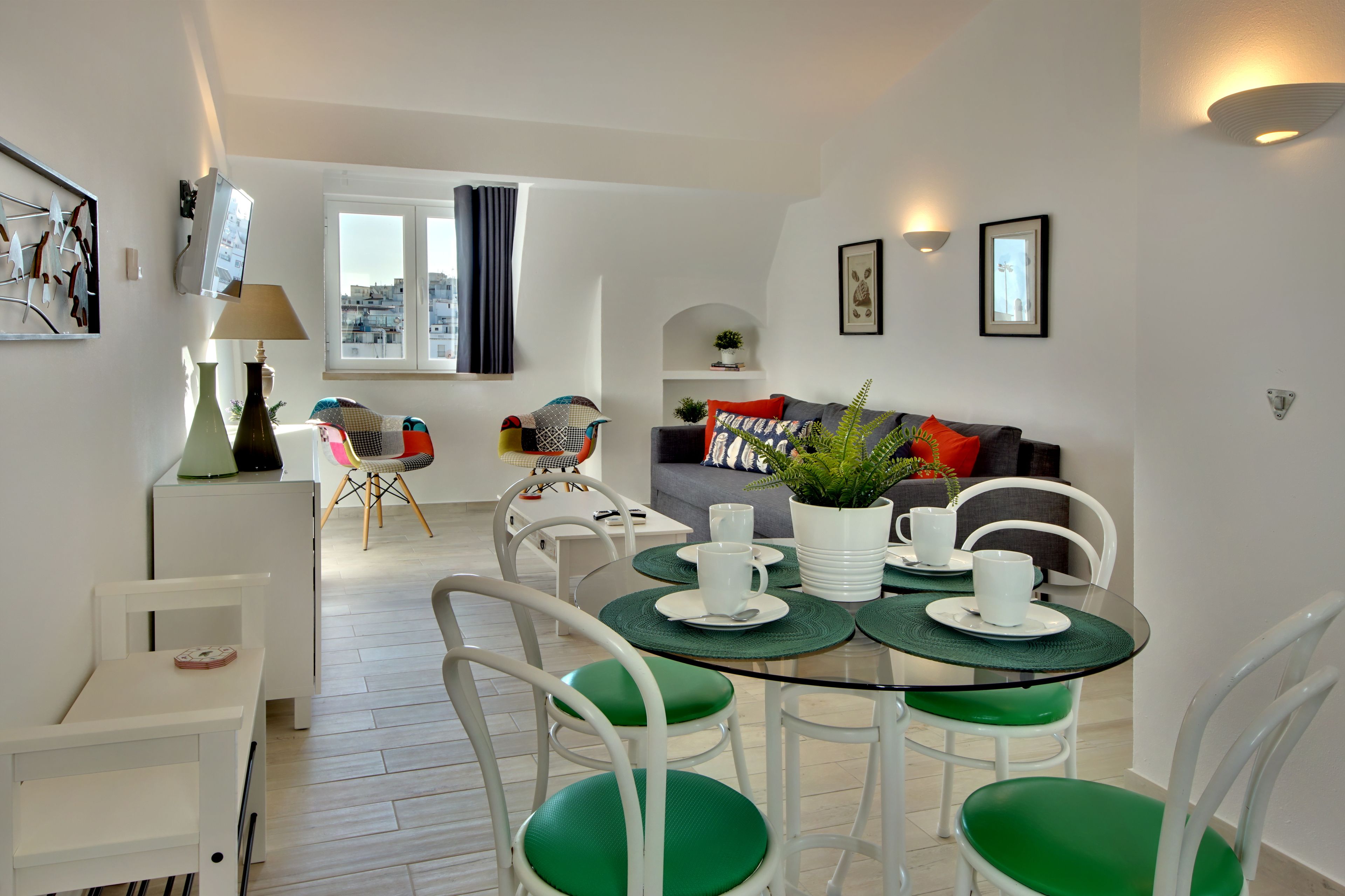 Un salon moderne avec un coin repas, des meubles blancs et une vue sur la ville par la fenêtre.