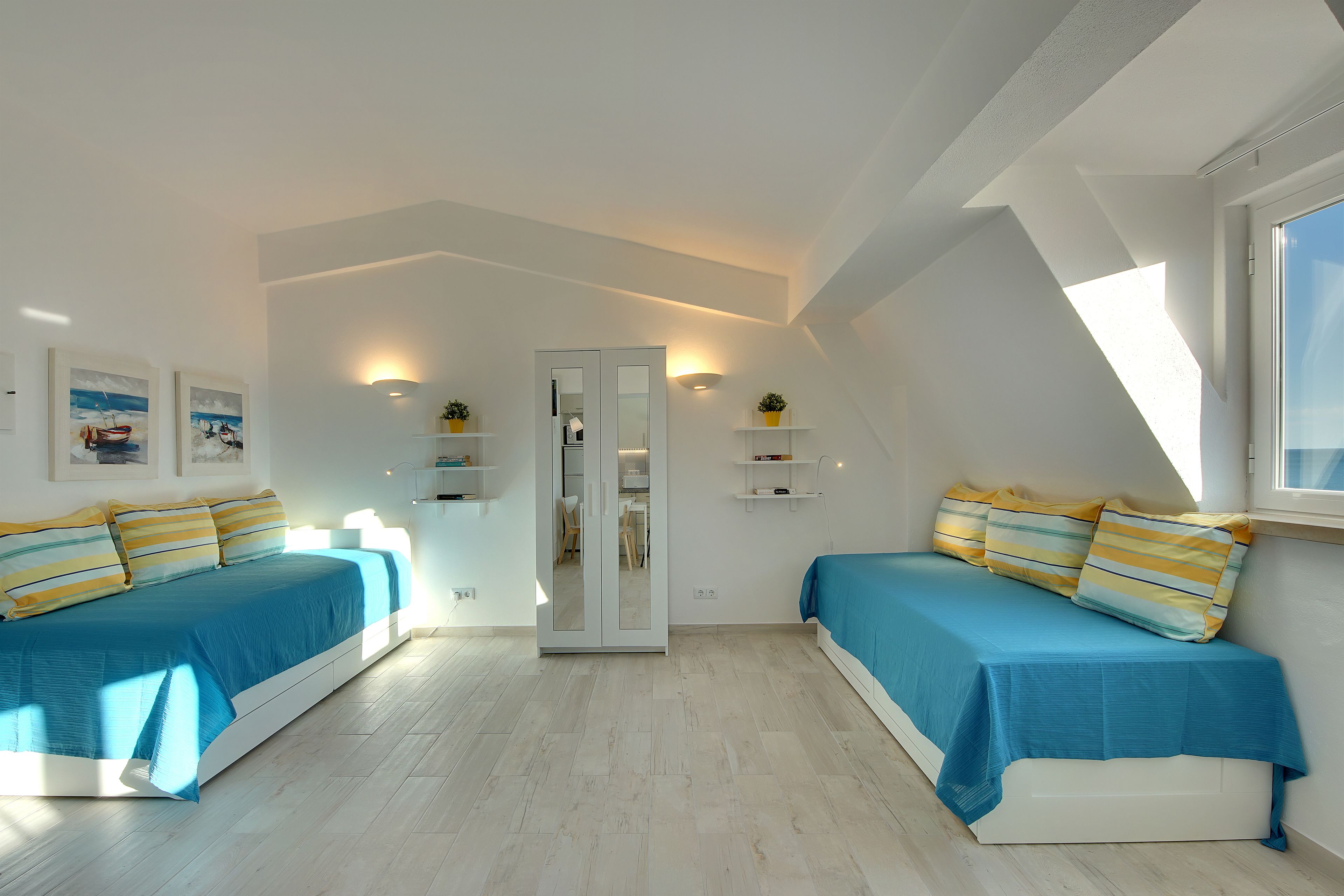 A modern bedroom with two beds, a large mirror, and a skylight.