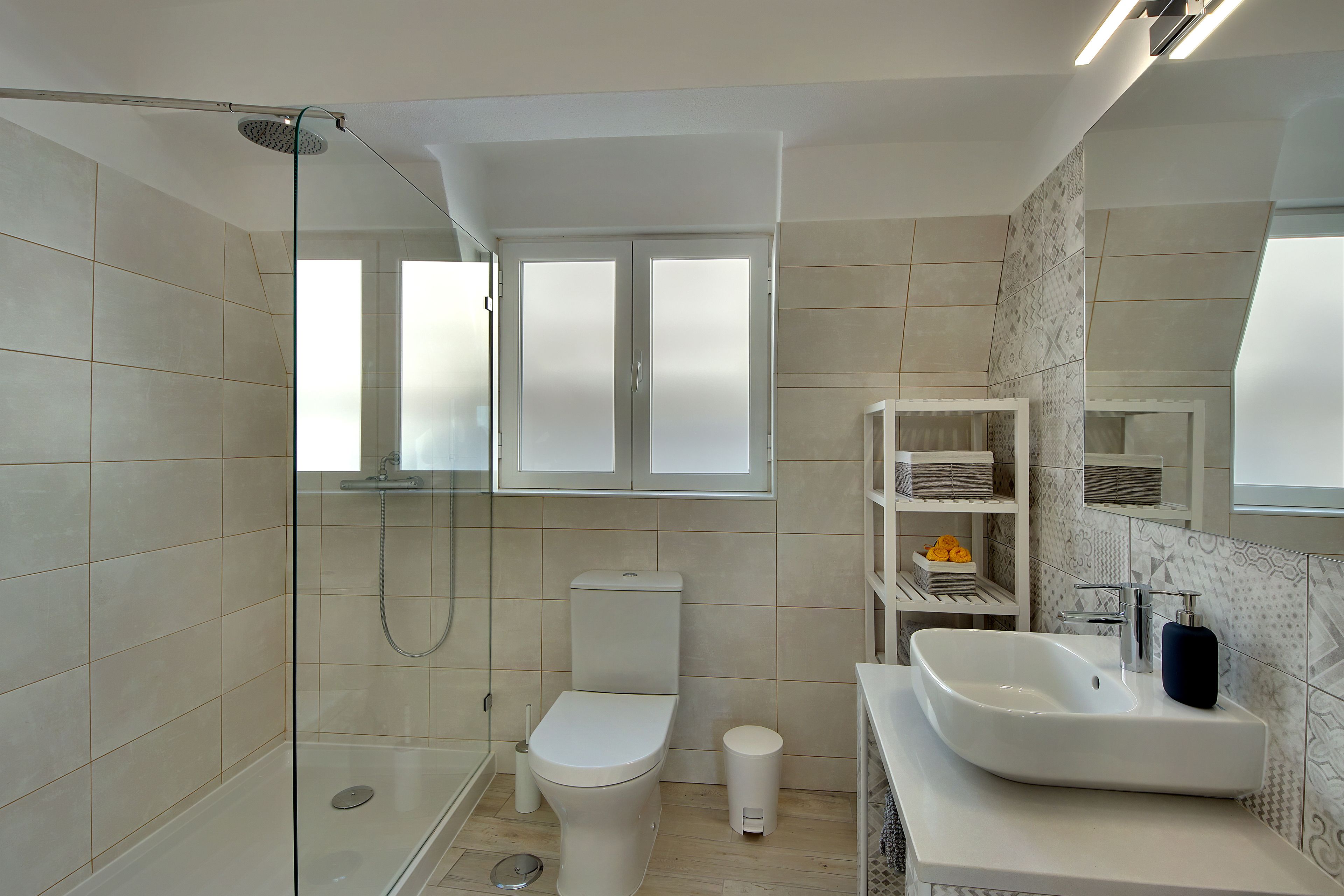 A modern bathroom with a glass-enclosed shower, a toilet, a sink with a mirror, and storage shelves.
