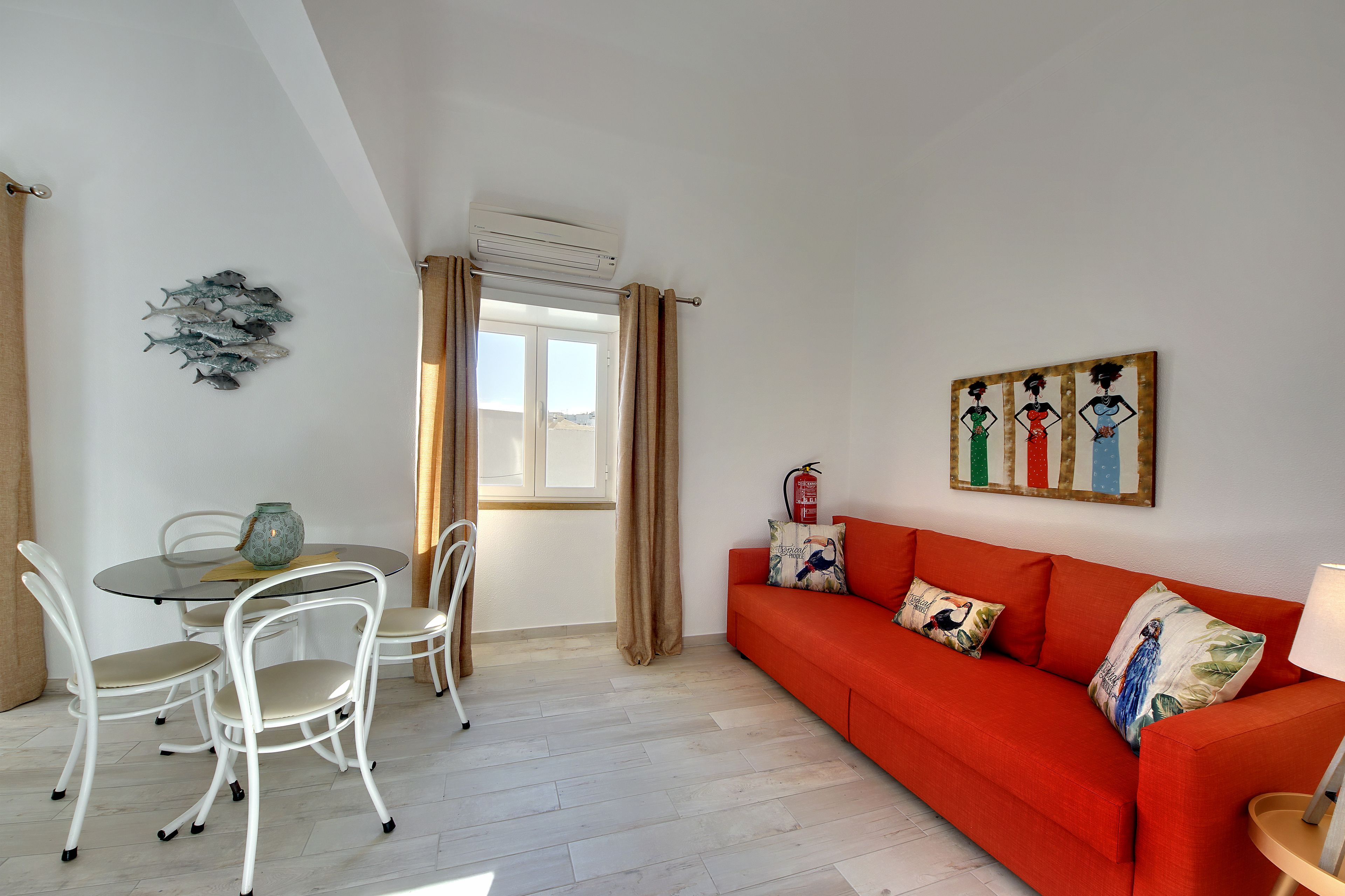 Een kamer met een eettafel, stoelen, een bank en een raam met gordijnen.