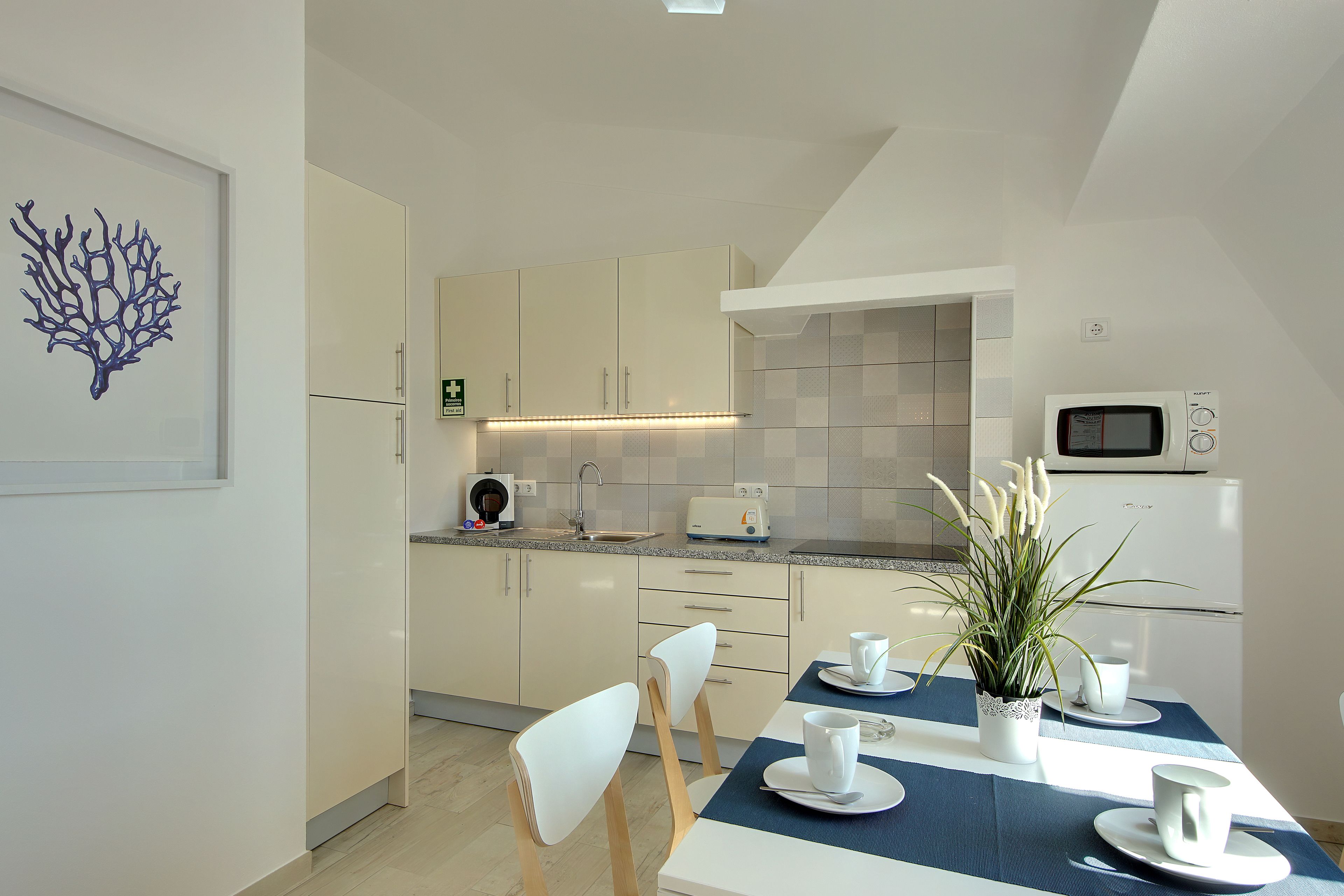A modern kitchen with white cabinets, a microwave, and a dining table set for two with white plates and cups.