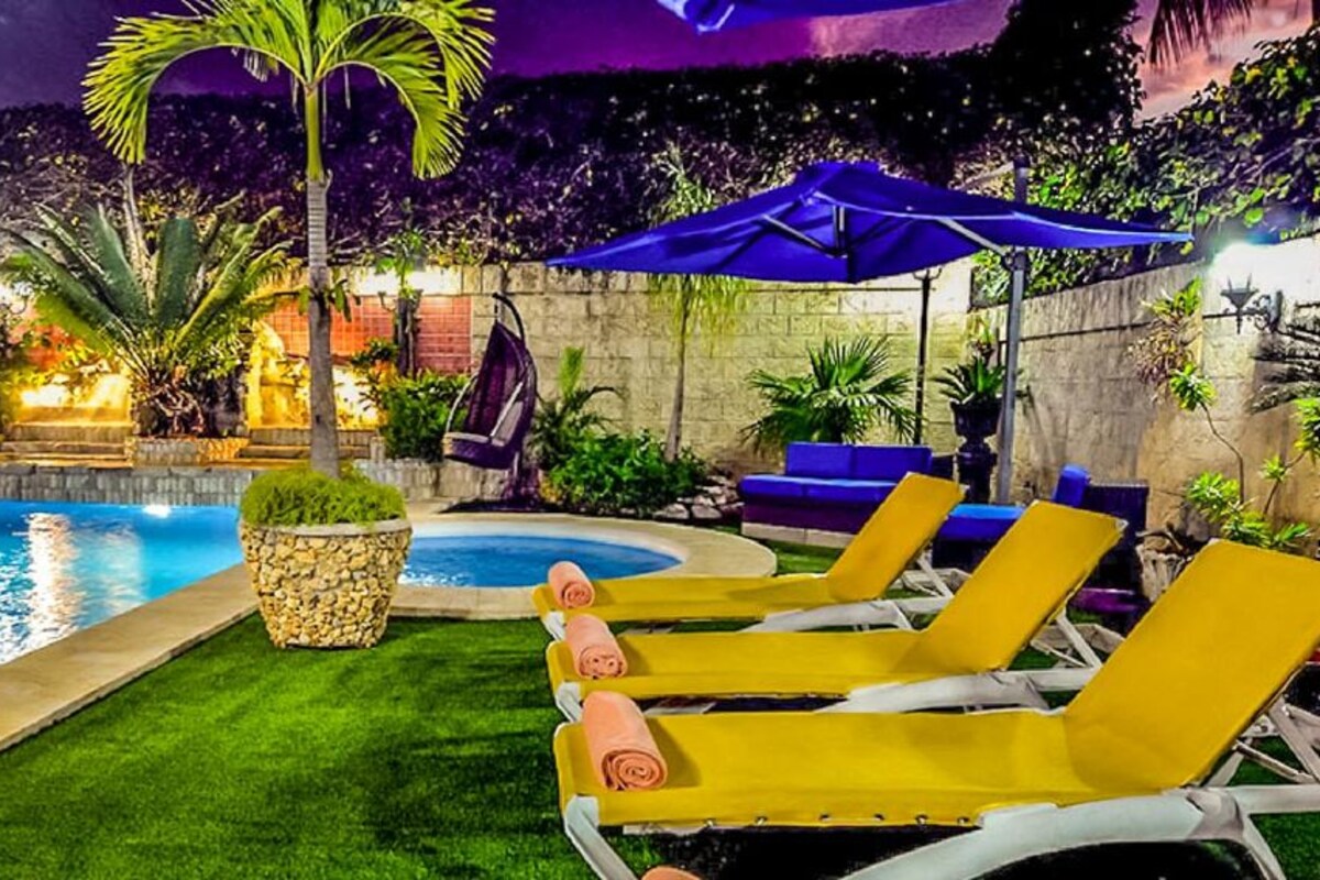 A pool area with lounge chairs, a stone planter, and a blue umbrella.
