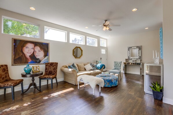 A spacious living room with a large window, a ceiling fan, and a cozy seating area with a sofa and chairs.