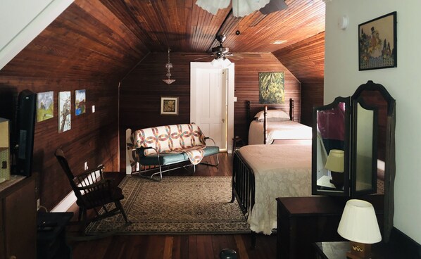 A cozy attic bedroom with wooden walls, a bed, a chair, a small table, and a mirror. - Historic Farmhouse/privacy/breathtaking views -Facebook @Valley View Escape, LLC (Collinsville)