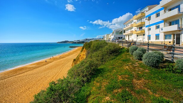 A coastal hotel with multiple balconies, a sandy beach, and a clear blue sky. - Inn the Beach Apartments (Albufeira)