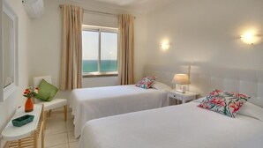 A hotel room with two beds, a small table with a vase, a bench, and a view of the sea. - Inn the Beach Apartments (Albufeira)