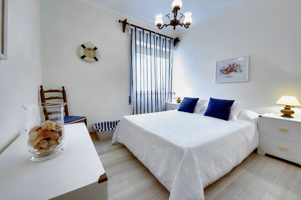 A bedroom with a bed, bedside table, lamp, chair, and a decorative glass vase.