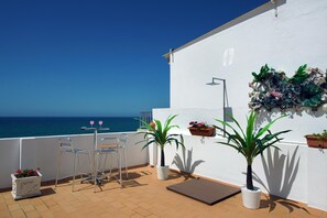A terrace with a view of the sea, featuring two chairs, a table, and potted plants. - Inn the Beach Apartments (Albufeira)