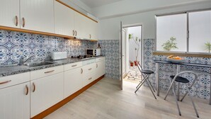 A modern kitchen with white cabinets, a patterned backsplash, and a dining area with two chairs and a table. - Inn the Beach Apartments (Albufeira)