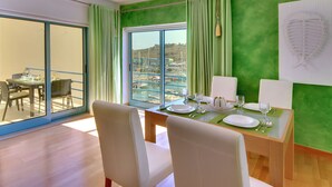 A dining area with a table set for two, a green wall, and a view of boats through a large window.