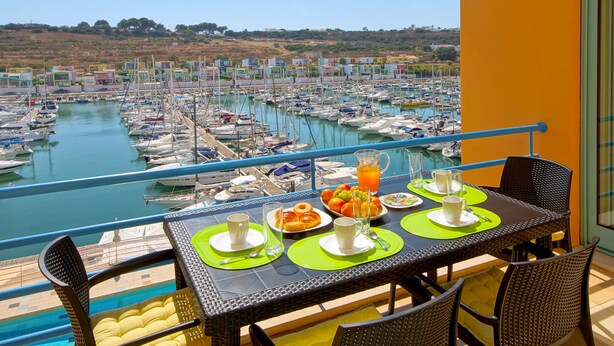 A balcony table with breakfast items and a view of a marina.