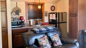 A kitchen with a microwave, coffee maker, and refrigerator. There is a dining area with a leather couch and pillows.
