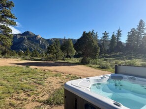 Un bain Ă remous avec vue sur les montagnes, entourĂ© dâarbres et bordĂ© dâun sentier de terre.