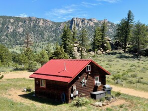 A wooden cabin with a red roof, a star decoration, and a small porch area.