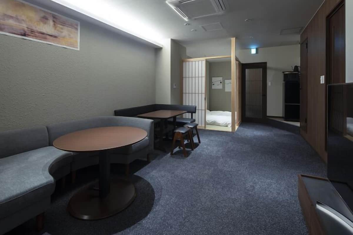 Habitación de hotel pequeña y funcional con sofá, una mesita redonda, un armario y una puerta corredera que da a la cama.