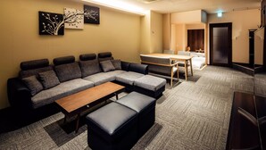 A modern living room with a sectional sofa, a wooden coffee table, and a small dining table. - Randor Residence Hiroshima Suites (Hiroshima)