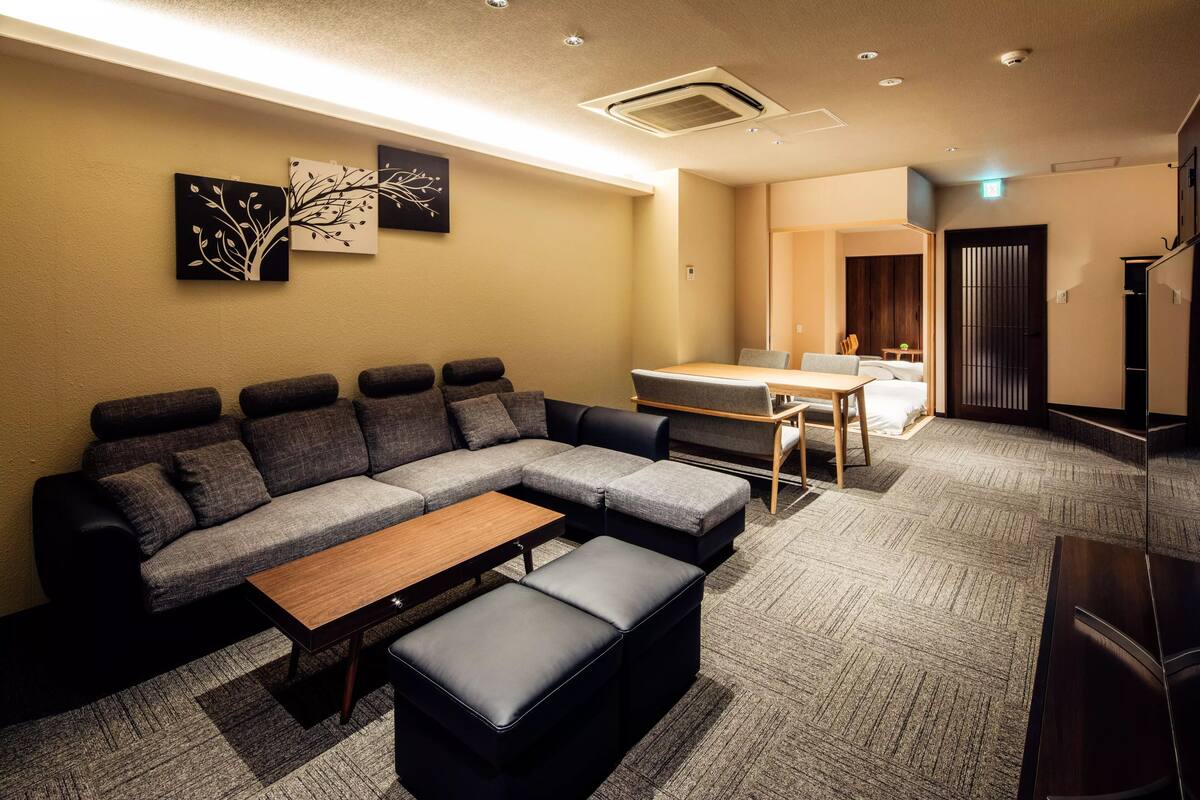 A modern living room with a sectional sofa, a wooden coffee table, and a small dining table.