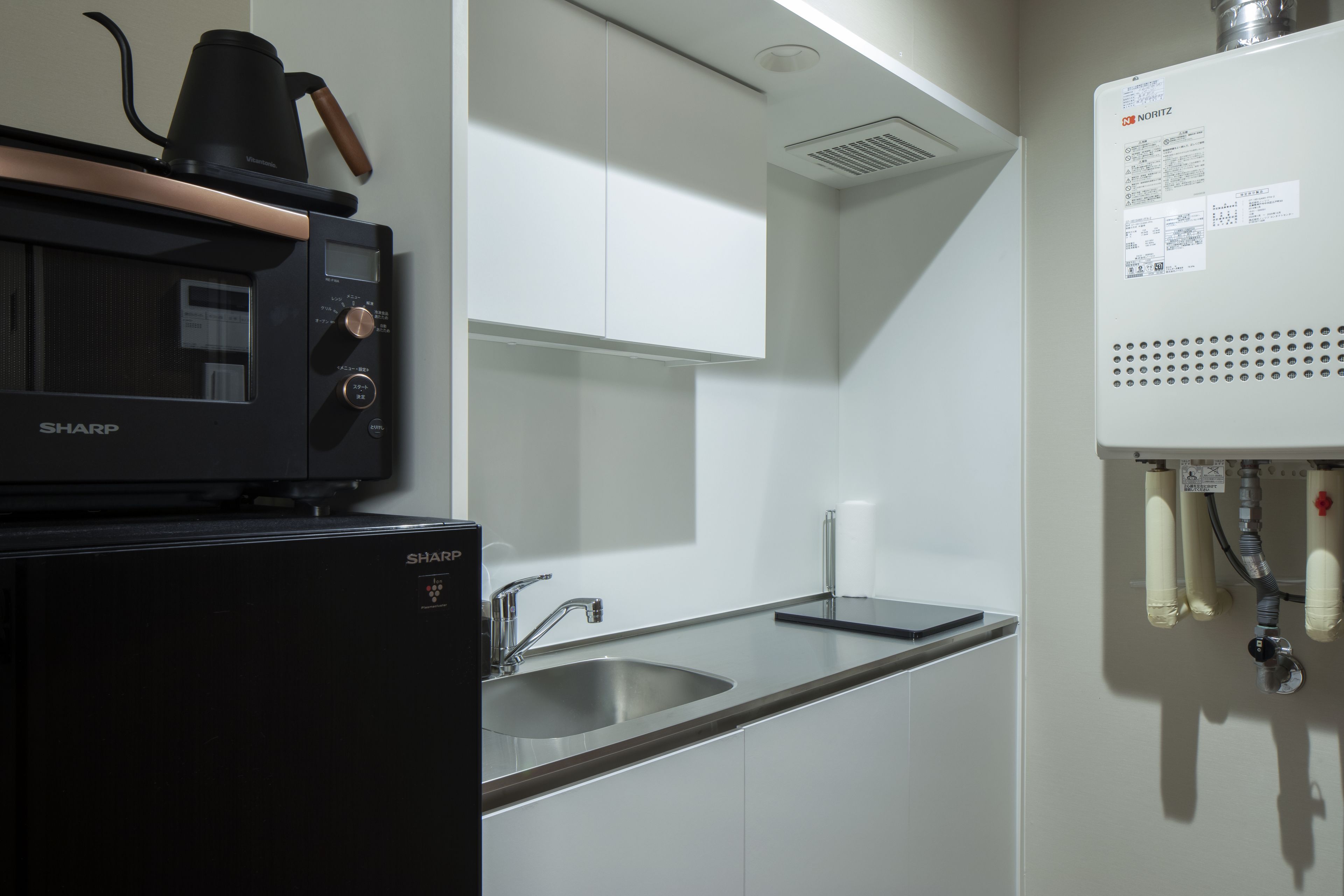 A modern kitchen with a Sharp microwave, stainless steel sink, and a water heater.