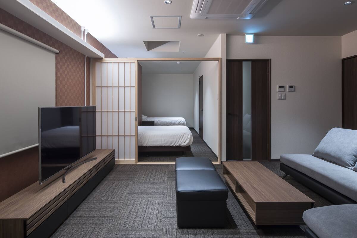 A modern hotel room with a flat-screen TV, a sofa, a bed, and a small table.