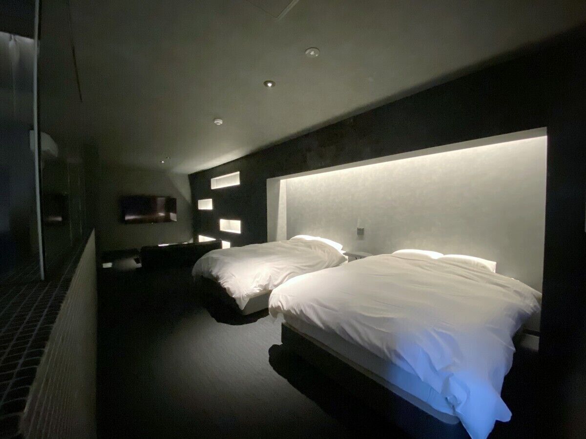 A modern hotel room with two beds, a dark floor, and recessed ceiling lighting.