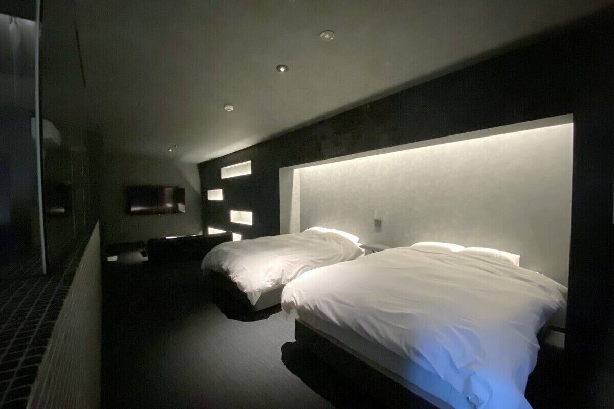 A modern hotel room with two beds, a dark floor, and recessed ceiling lighting.