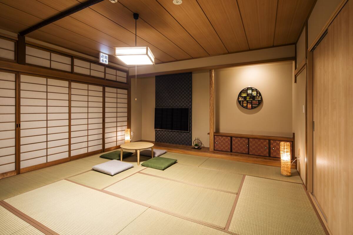 A traditional Japanese room with tatami flooring, a low table with cushions, a shoji screen, and a hanging scroll.