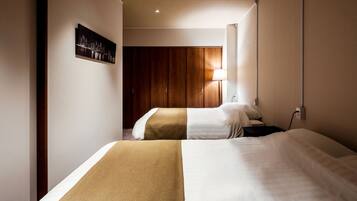 Una habitación de hotel con dos camas, un armario de madera, una mesita de noche y una lámpara de pared.