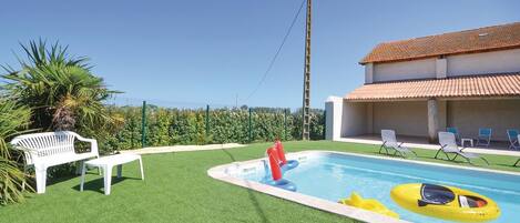 Una piscina con flotadores, un porche techado con sillas y una palmera.