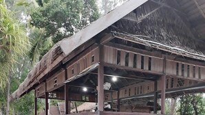 A wooden structure with a thatched roof, elevated on stilts, surrounded by sand and palm trees. - Andau Homestay (Saprokren)