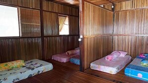 A room with wooden walls and floors, two single beds with floral bedding, a window, and a door. - Andau Homestay (Saprokren)