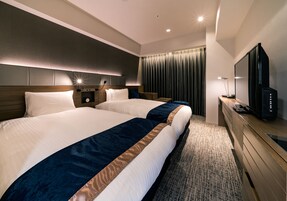Habitación de hotel con dos camas, televisión, escritorio y un ventanal grande con cortinas.
