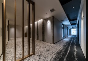 A modern hotel corridor with a number '5' on the wall, wooden paneling, and a carpeted floor.