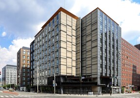 Un hôtel moderne, situé dans un immeuble d’angle, avec de nombreux étages et une entrée imposante.