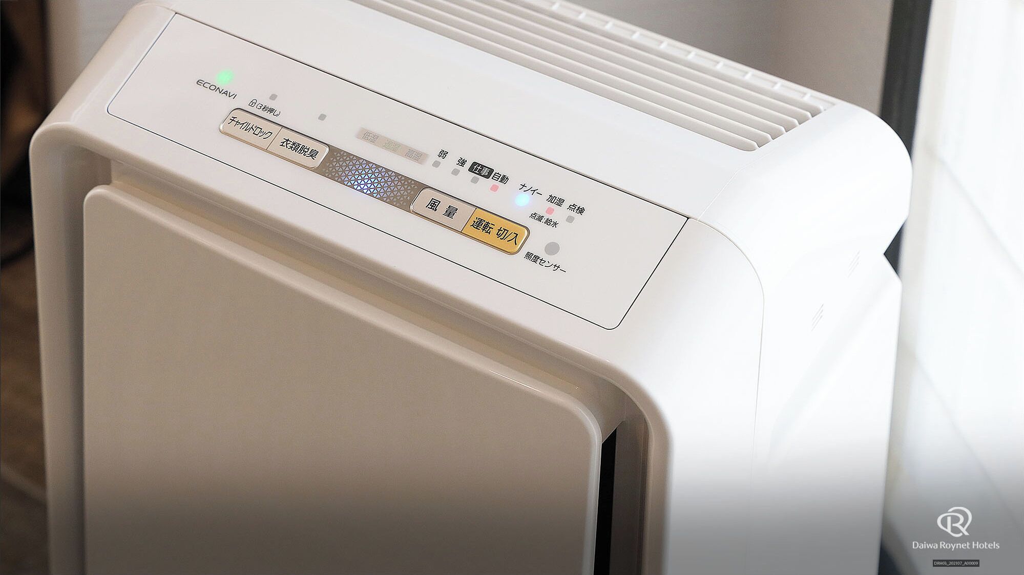 Um purificador de ar branco com um painel de controle com texto em japonês e um botão de energia.