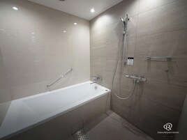 A modern bathroom with a bathtub, a shower, and a handrail.
